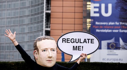 An activist of environmental NGO Avaaz wearing a mask depicting Facebook CEO Mark Zuckerberg holds a banner reading "Regulate me" during an action marking the release of the Digital Services Act, outside the European Commission
